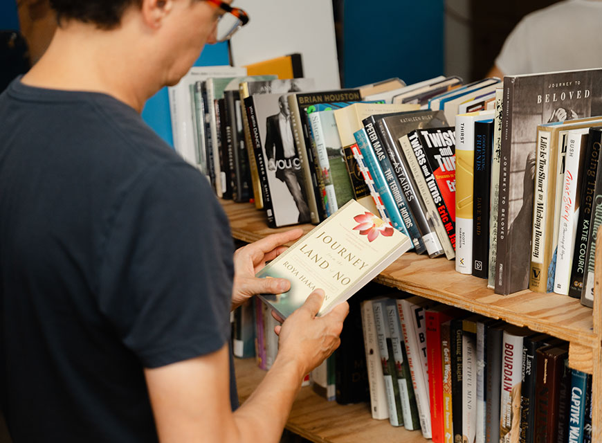 Man holding a book in front of library shelves.