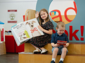 Two children sitting in the children's section of a library reading books.