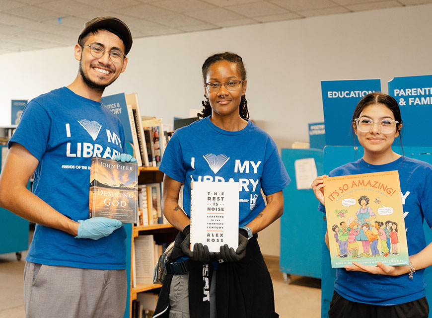 Group of volunteers wearing "I love my library" shirts and holding up books.