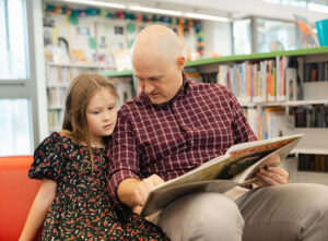 Man and young girl reading a book together at the library.