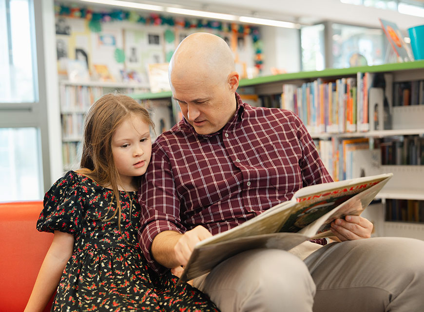 Man and young girl reading a book together at the library.