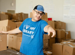 Man in a "I love my library" shirt directing volunteers moving boxes.