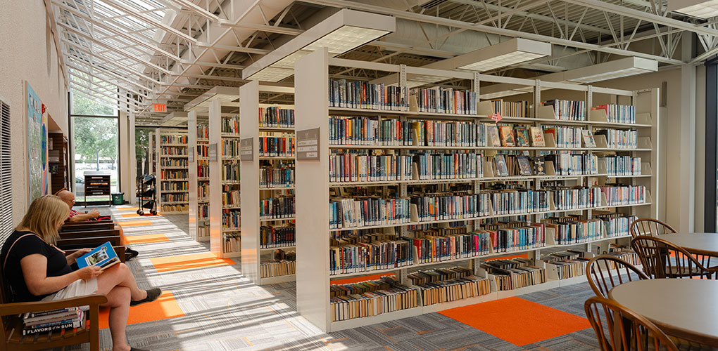 Interior view of a library with many shelves of books and people seated and reading.