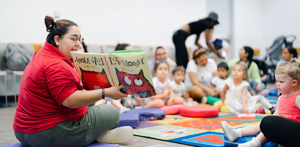 Volunteer reading a children's book to a group of young children.