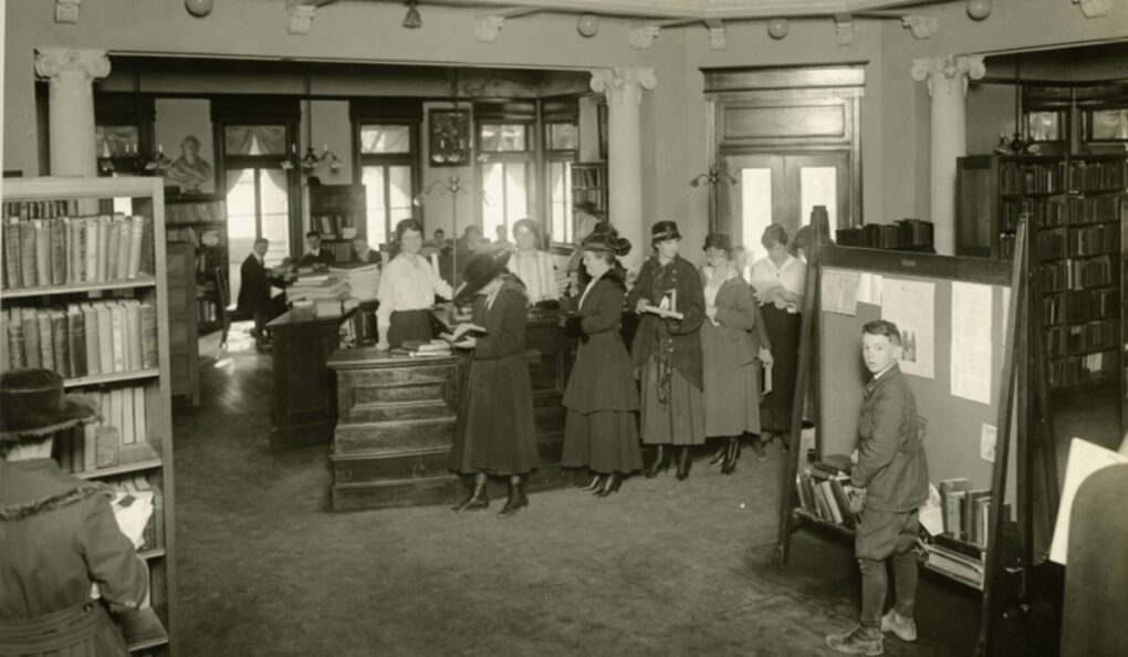 A historical black and white photo of people in line to check out books at the Houston Lyceum.
