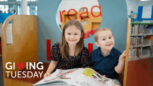 Two children smiling at the Collier Branch Library of the Houston Public Library system while holding an open book.